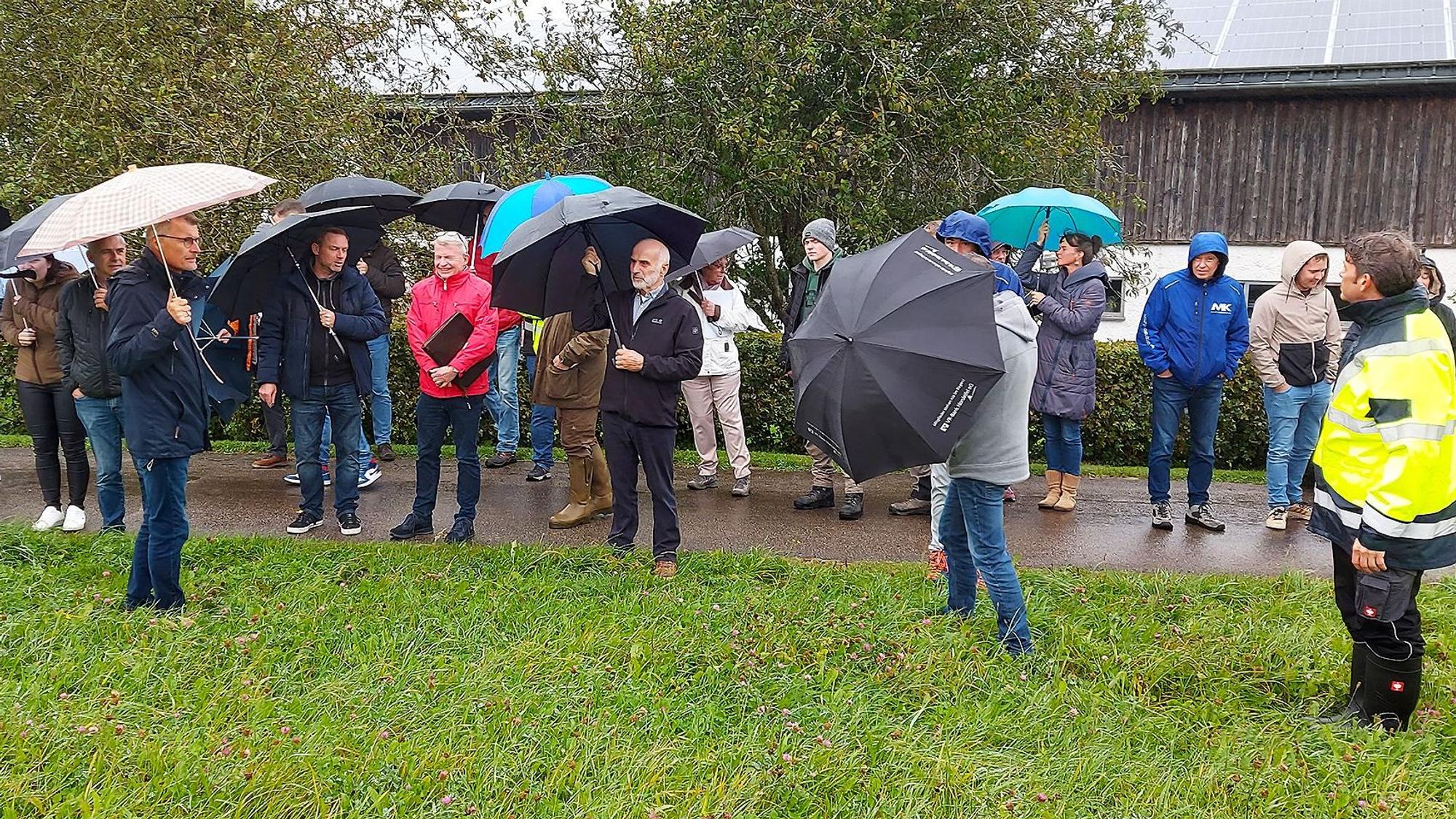 Mehrere Teilenehmer des Ortstermins stehen mit Schirmen und in Regenjacken auf einer Wiese.