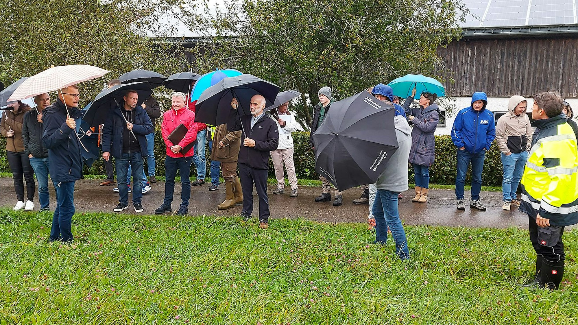 Mehrere Teilenehmer des Ortstermins stehen mit Schirmen und in Regenjacken auf einer Wiese.