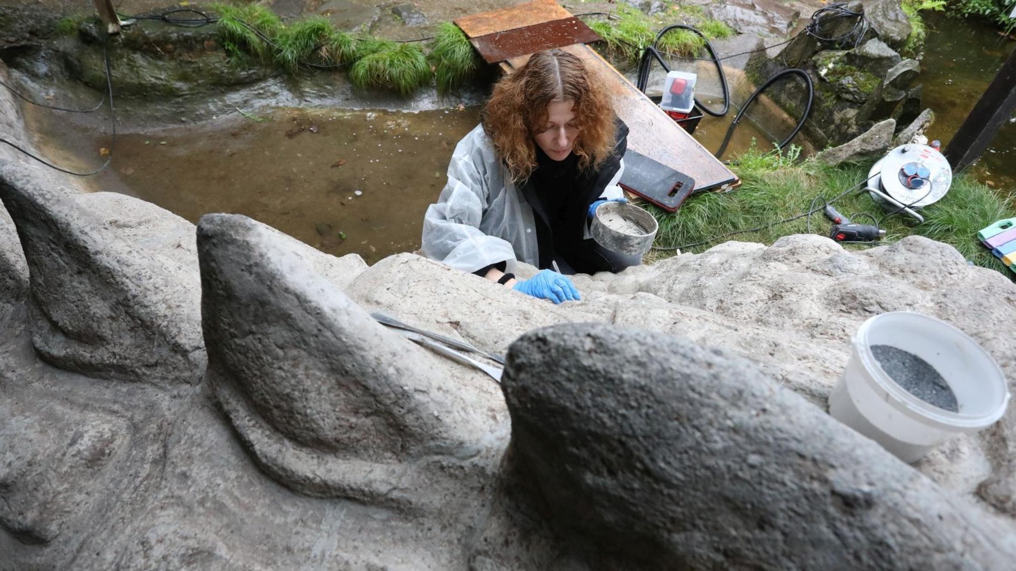 Eine Frau arbeitet mit Werkzeug an einer großen Betonfigur, die einen Drachen darstellt.