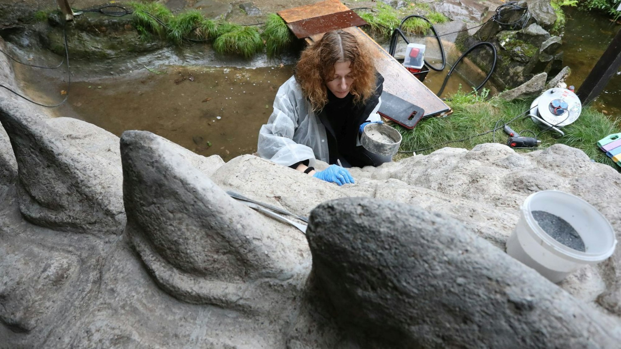 Eine Frau arbeitet mit Werkzeug an einer großen Betonfigur, die einen Drachen darstellt.