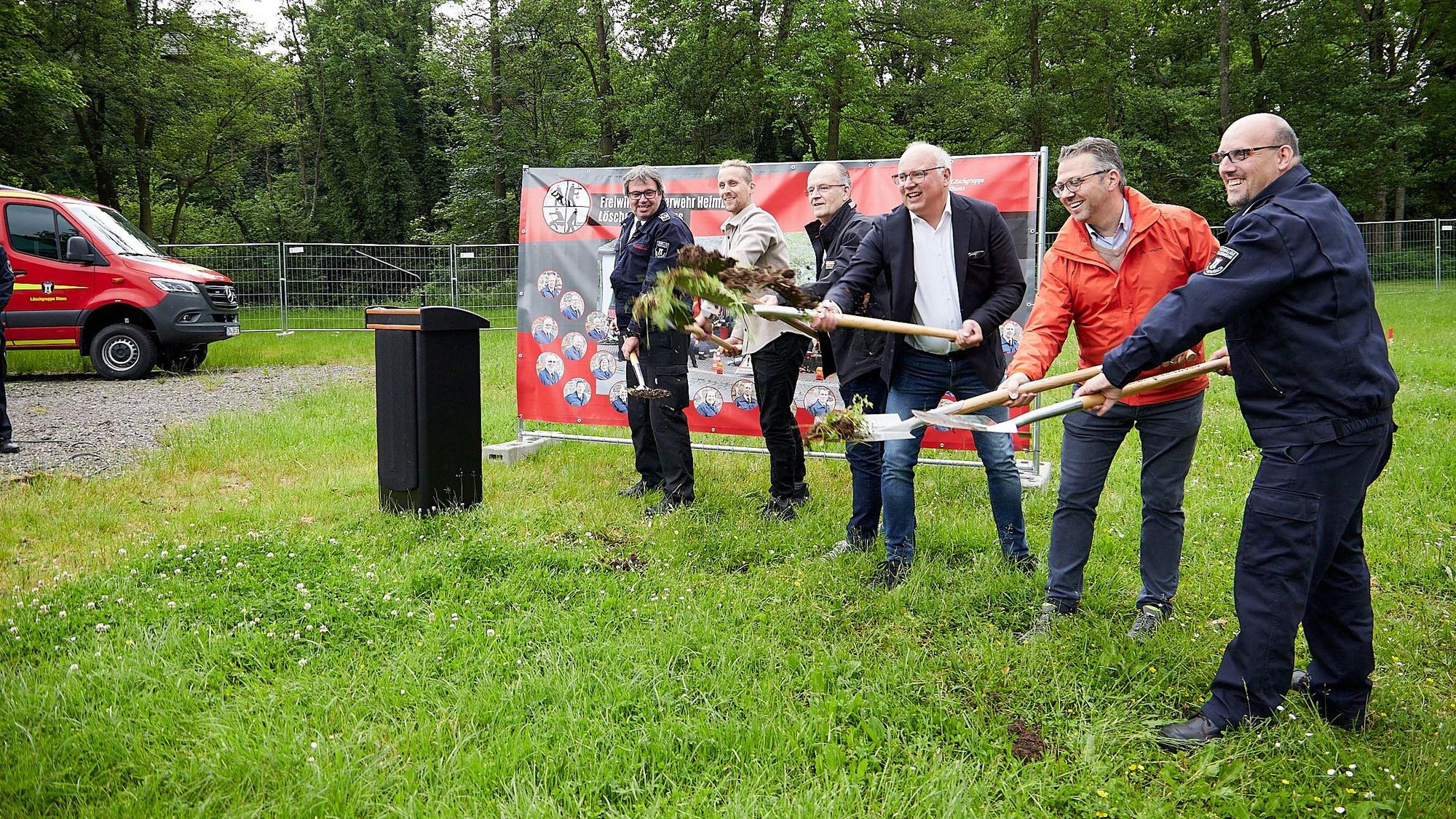 Mehrere Personen beim symbolischen Spatenstich auf einer Wiese.