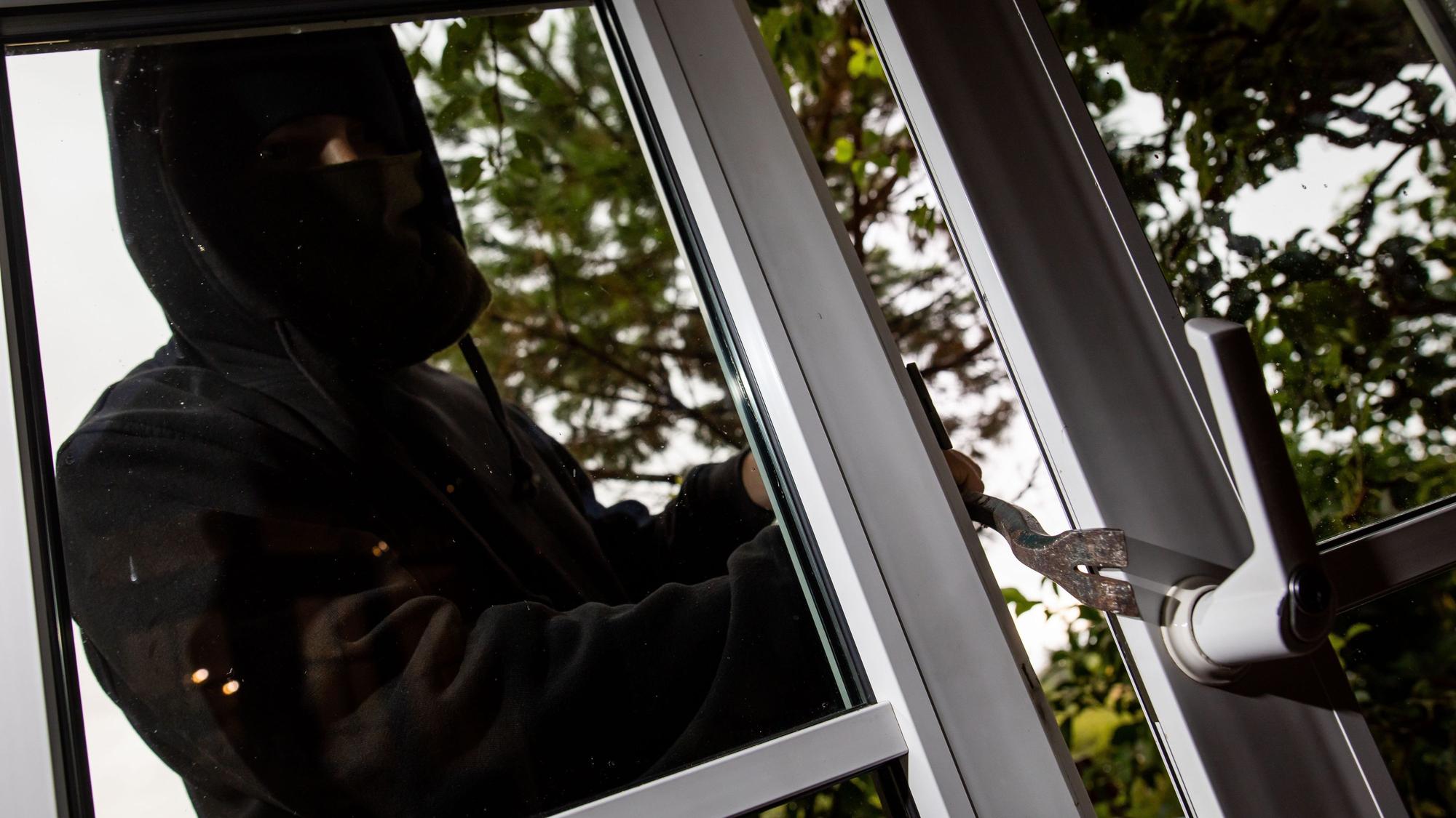 Das Bild zeigt eine maskierte Person vor einem Fenster.
