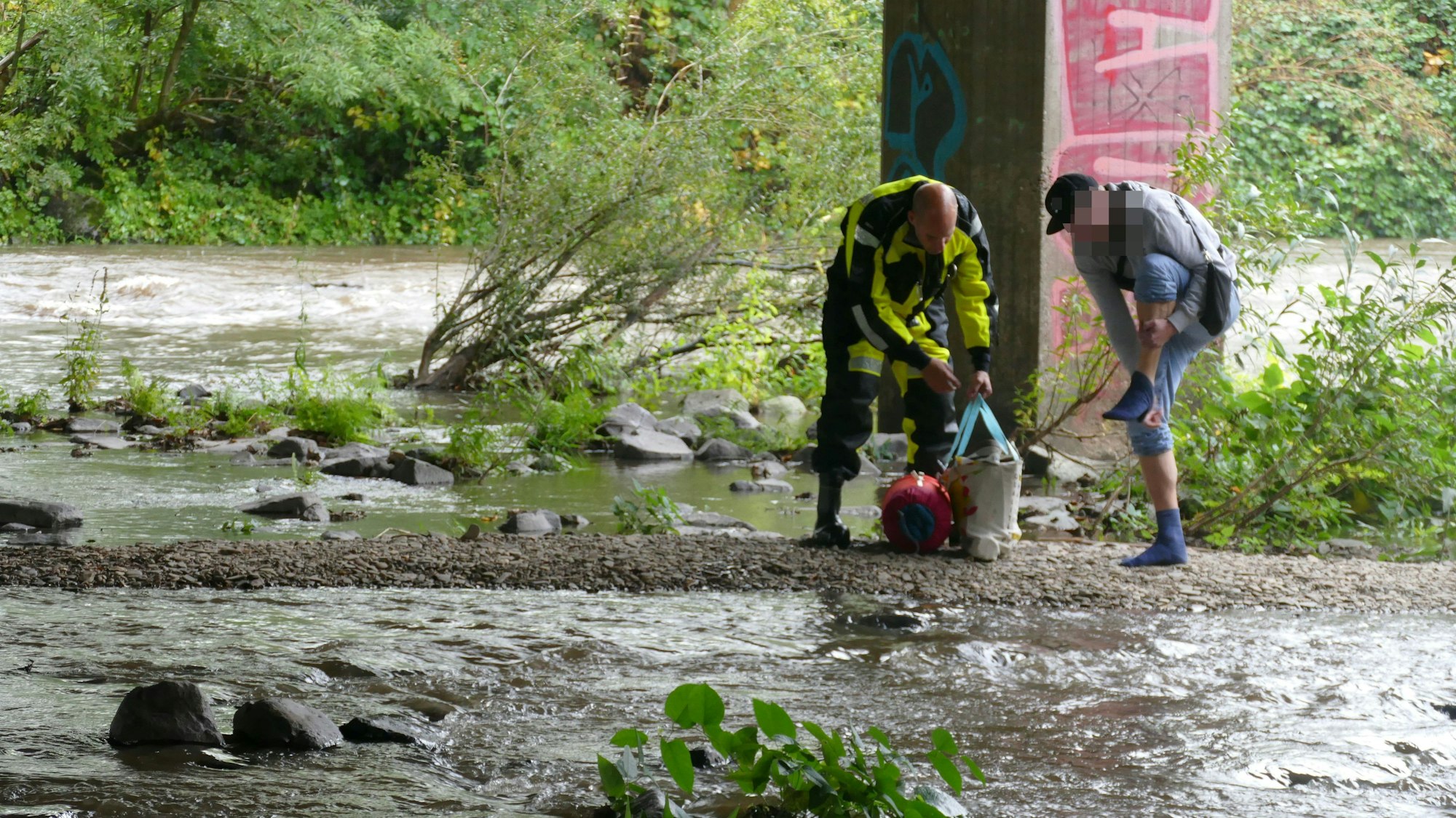 Ein Mann zieht seine Schuhe aus, ein Feuerwehrmann im Überlebensanzug nimmt eine Tasche.