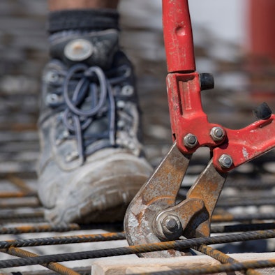 Mit einem Bolzenschneider schneiden Handwerker auf dem Rohbau eines Mehrfamilienhauses Stahlmatten auf die richtige Größe.