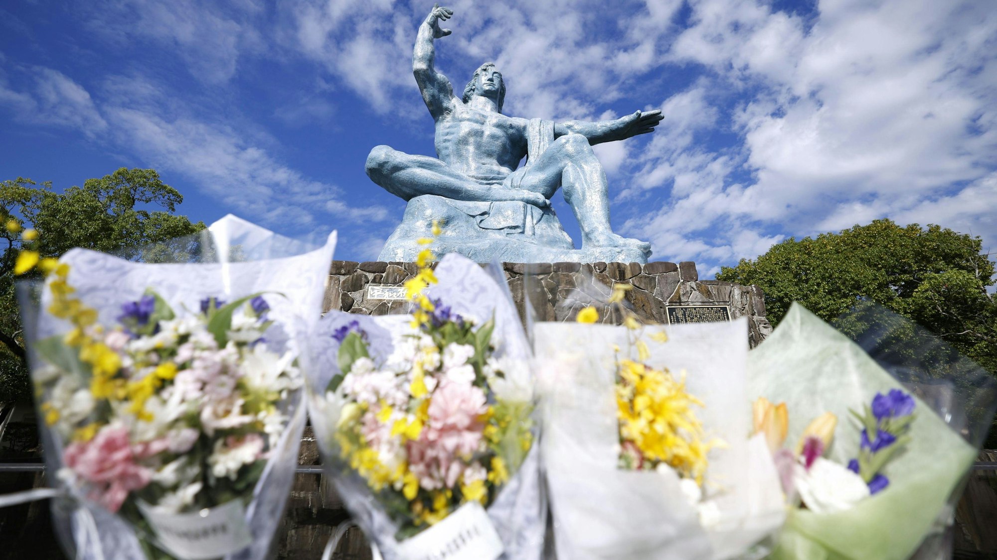 11.10.2024, Japan, Nagasaki: Blumensträuße liegen vor der Friedensstatue im Friedenspark in Nagasaki, im Südwesten Japans. Die japanische Organisation Nihon Hidankyo von Überlebenden der Atomwaffenabwürfe auf die Städte Hiroshima und Nagasaki wird in diesem Jahr mit dem Friedensnobelpreis geehrt, wie das norwegische Nobelkomitee in Oslo bekanntgab. Foto: ---/kyodo/dpa +++ dpa-Bildfunk +++