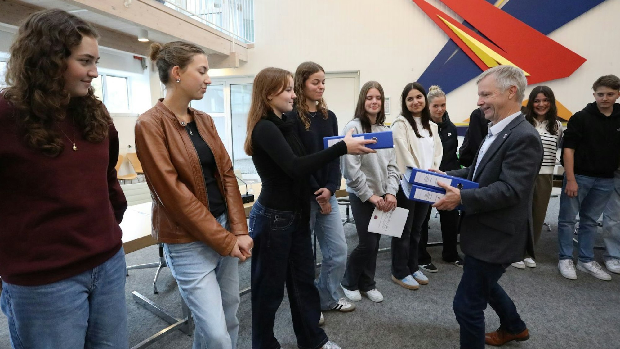 Eine Gruppe von jungen Leuten übergibt dem Bürgermeister drei blaue Aktenordner.