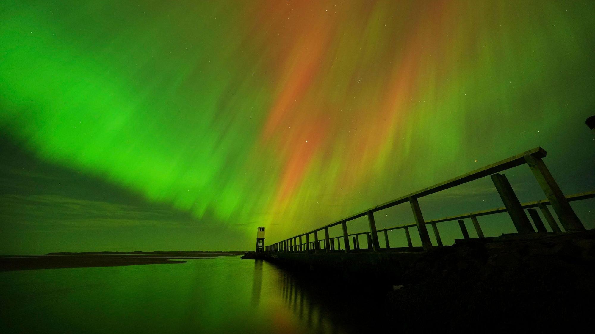 Nordlichter am Himmel über der Schutzhütte auf dem Damm, der zur Holy Island in Northumberland an der Nordostküste Englands führt, zu sehen.