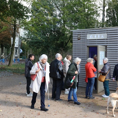 Eine Gruppe älterer Menschen vor einem Toilettenhäuschen.