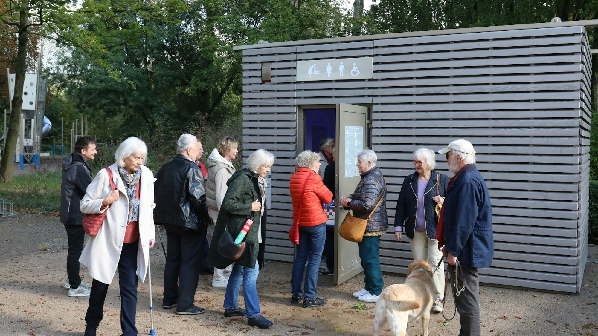 Eine Gruppe älterer Menschen vor einem Toilettenhäuschen.