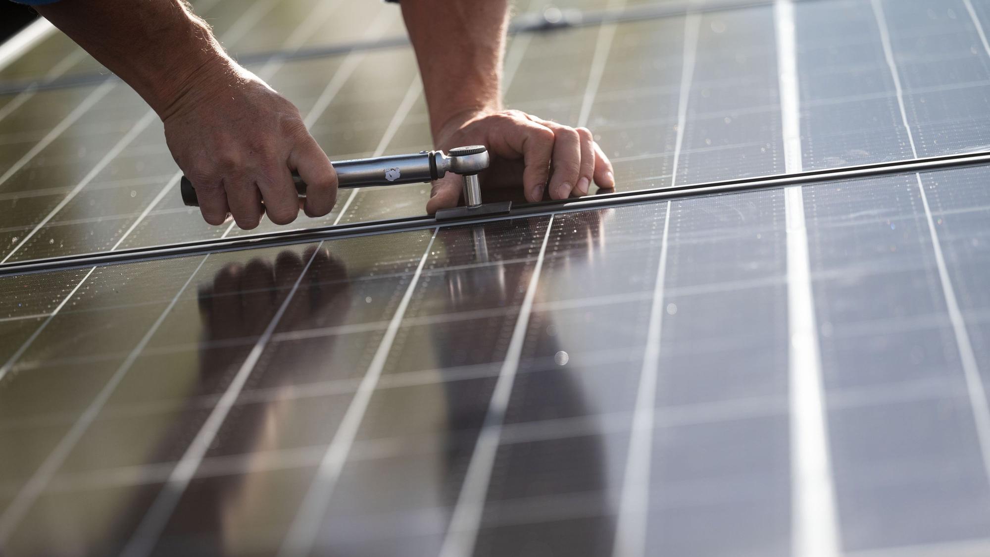 Ein Mitarbeiter einer Firma montiert Photovoltaikmodule auf dem Dach eines Hauses.