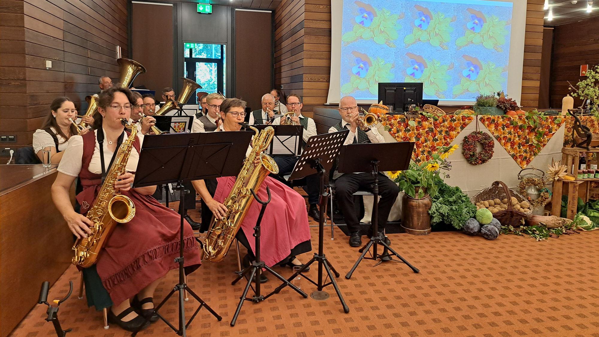 Musikerinnen und Musiker spielen auf Blasinstrumenten, rechts davon liegen Feldfrüchte und Äpfel als Deko.
