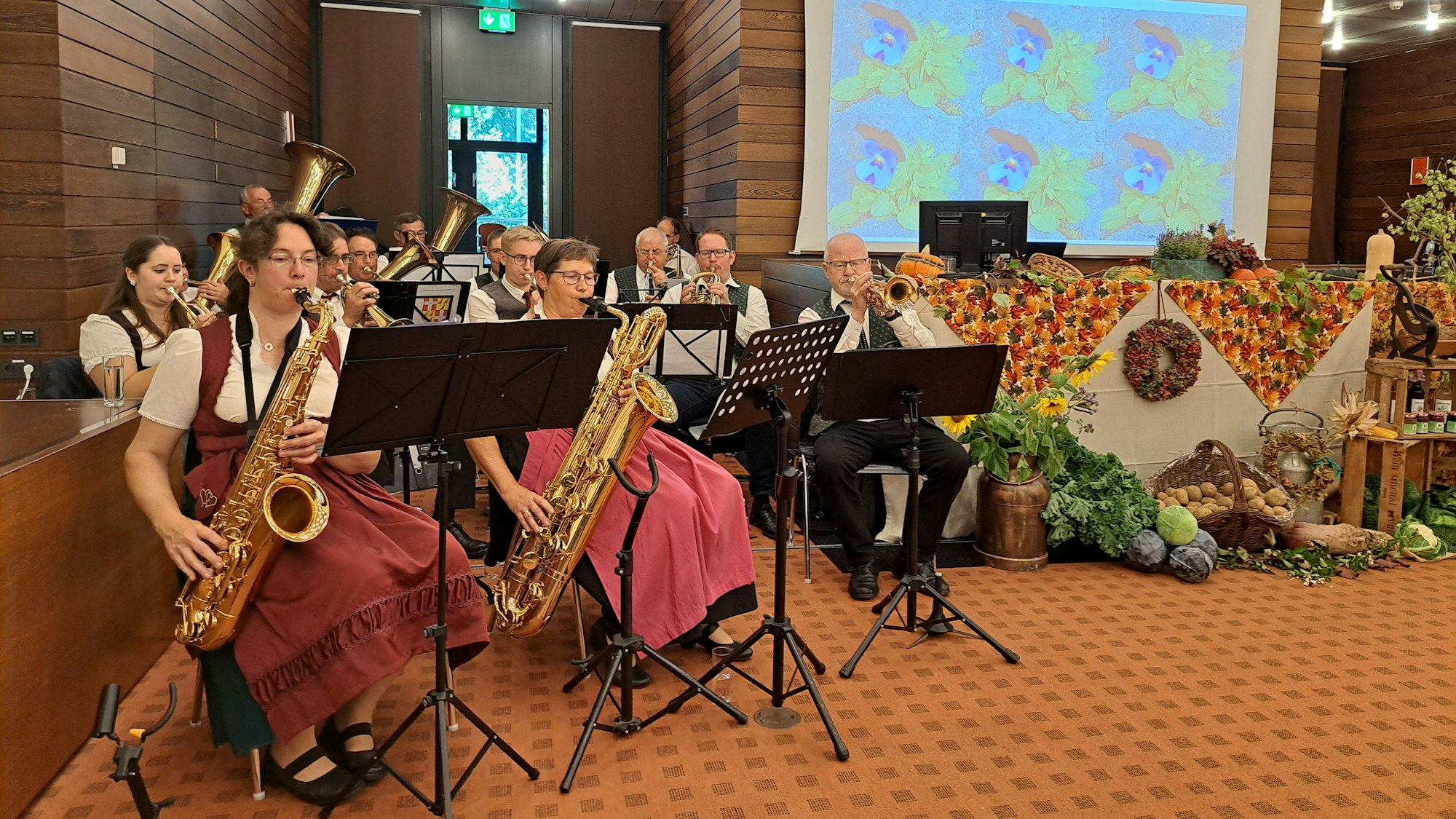 Musikerinnen und Musiker spielen auf Blasinstrumenten, rechts davon liegen Feldfrüchte und Äpfel als Deko.