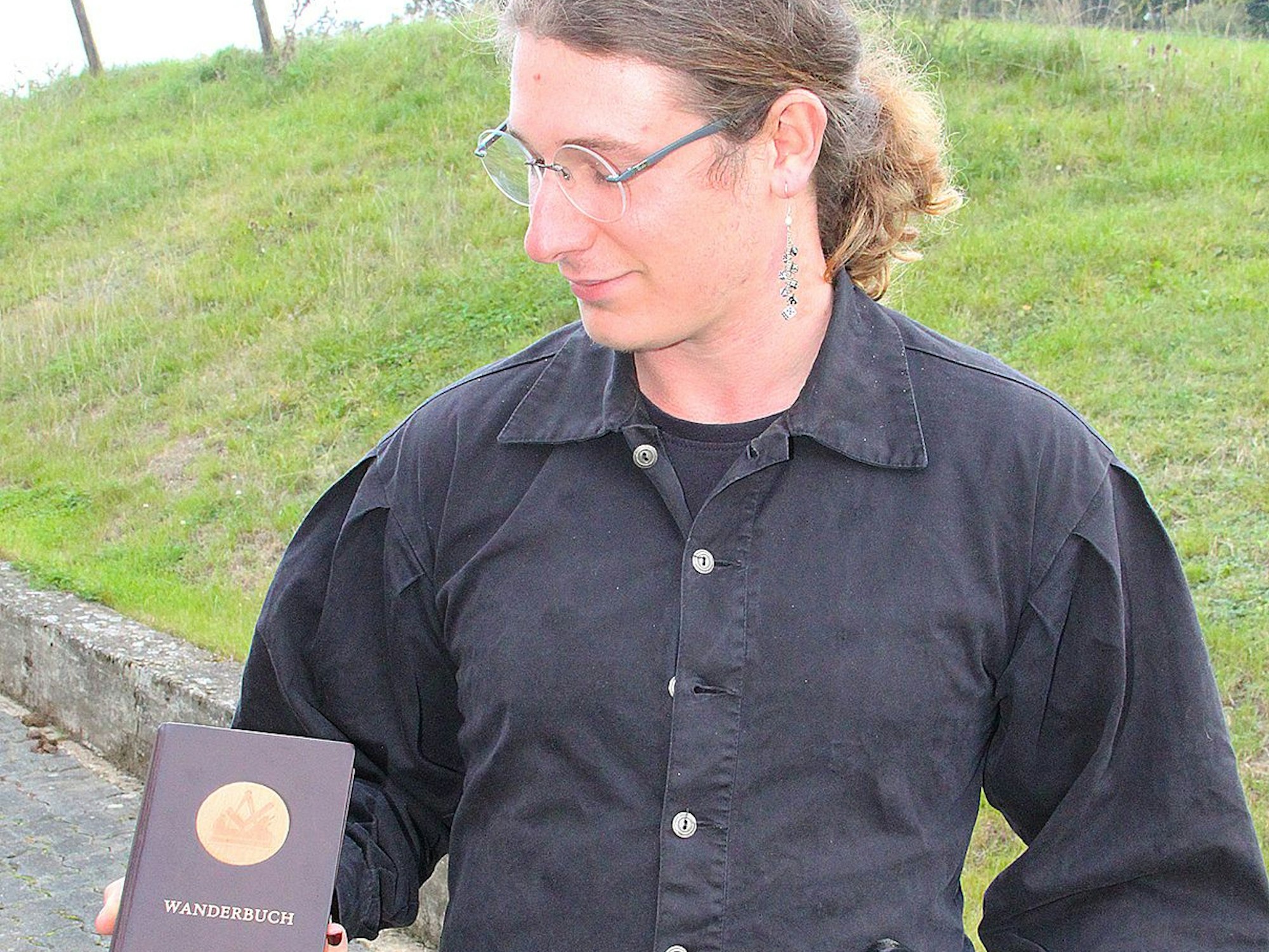 Ein junger Mann hält ein Wanderbuch.