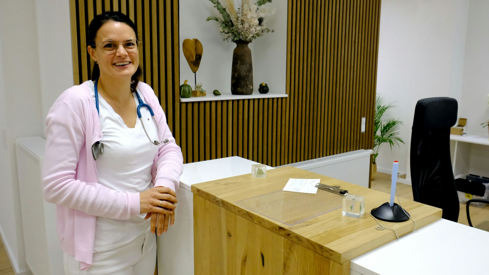 Dr. med. Ekatarini Karidas-Moitzheim steht am Empfang ihrer Praxis. Um ihren Hals hängt ein Stethoskop.