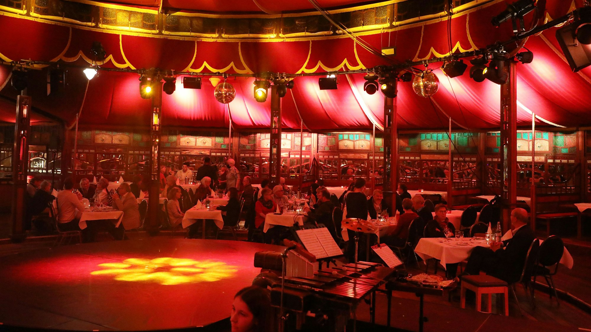 Menschen sitzen an Tischen im Altenberger Spiegelzelt, das in rotes Licht getaucht ist.