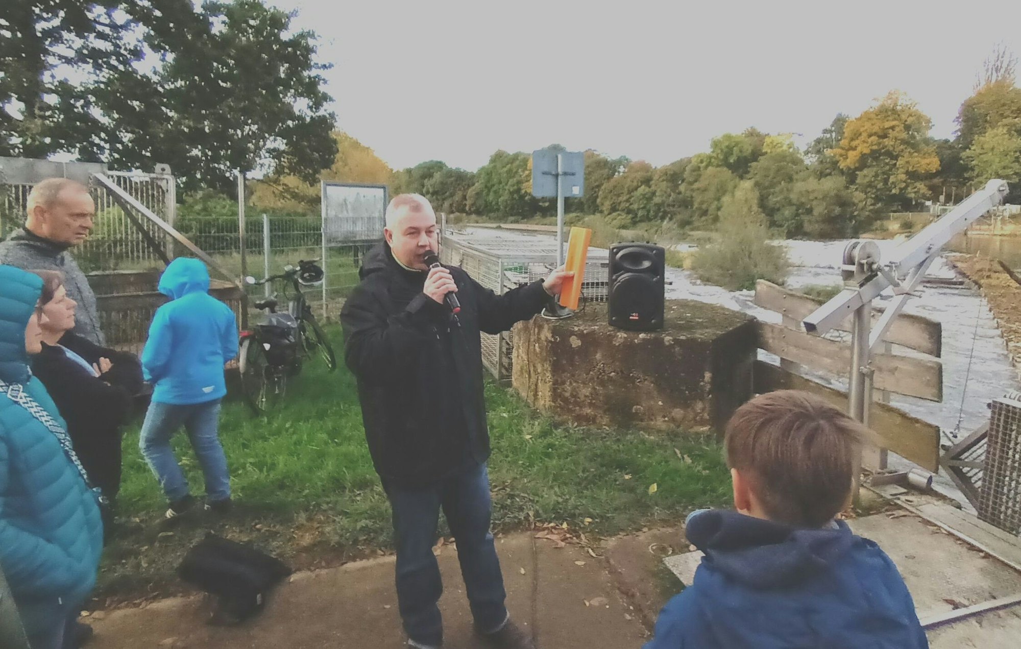 Ein Mann hält am Flussufer einen Vortrag vor Zuhörern