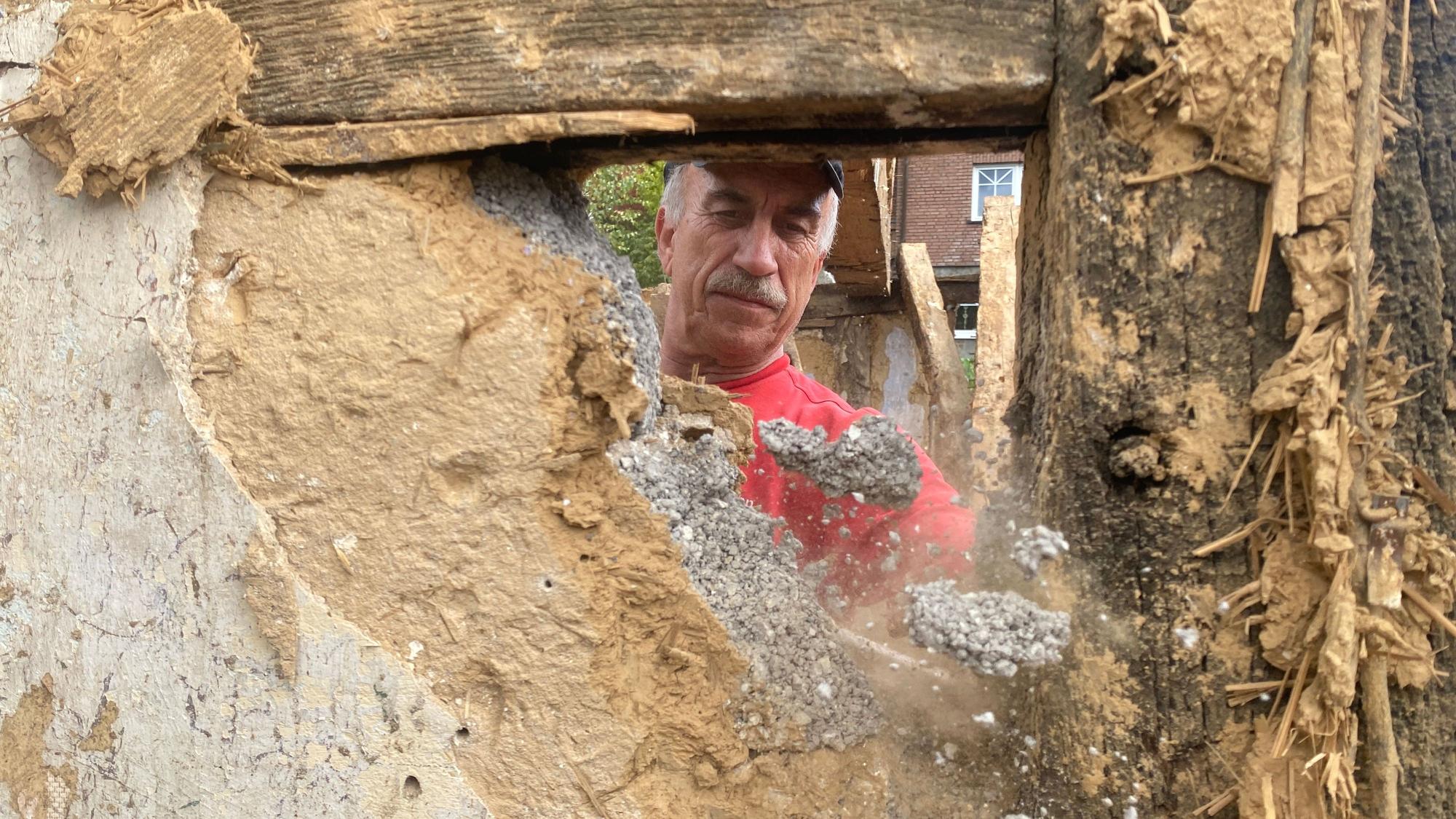 Ein Handwerker schlägt ein Loch in eine Lehm-Fachwerkwand.