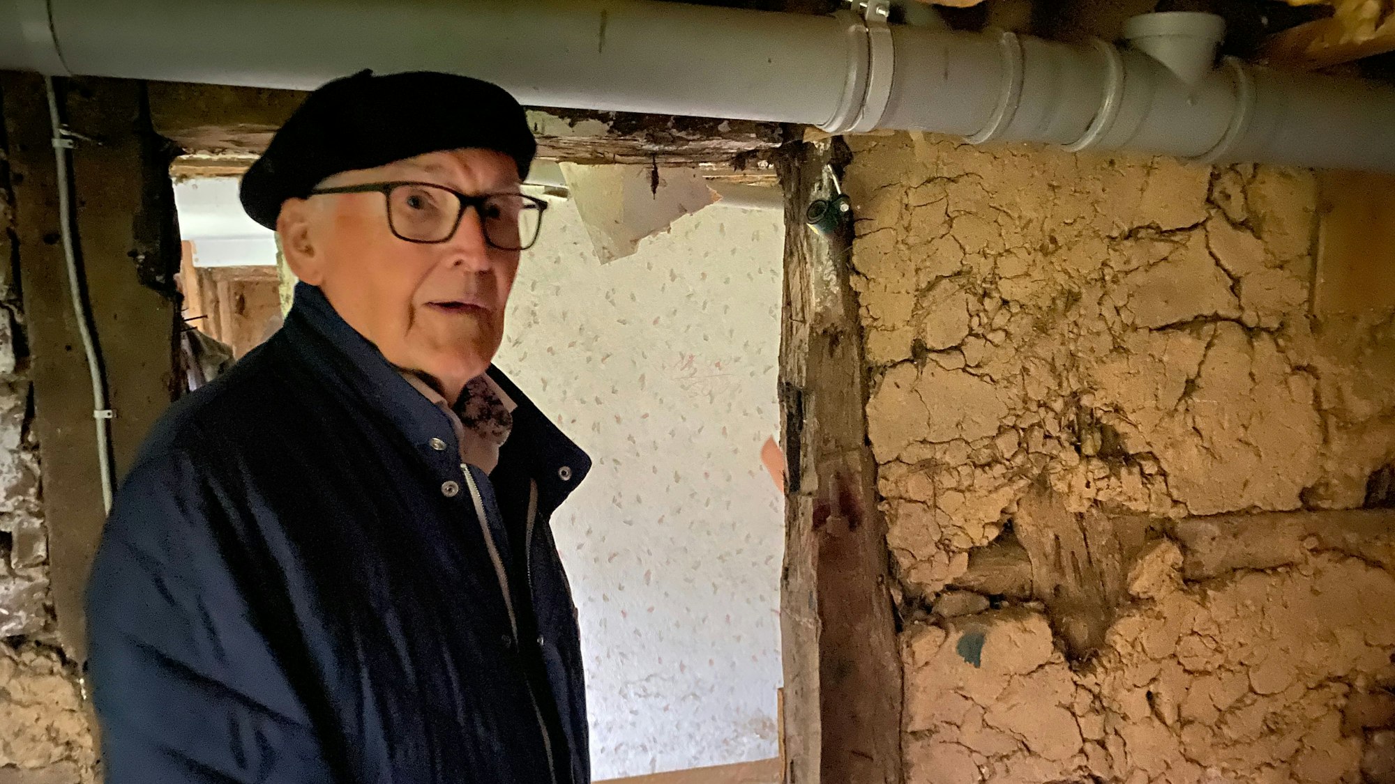Ein alter Mann vor einer Fachwerkwand mit Lehmgefache.