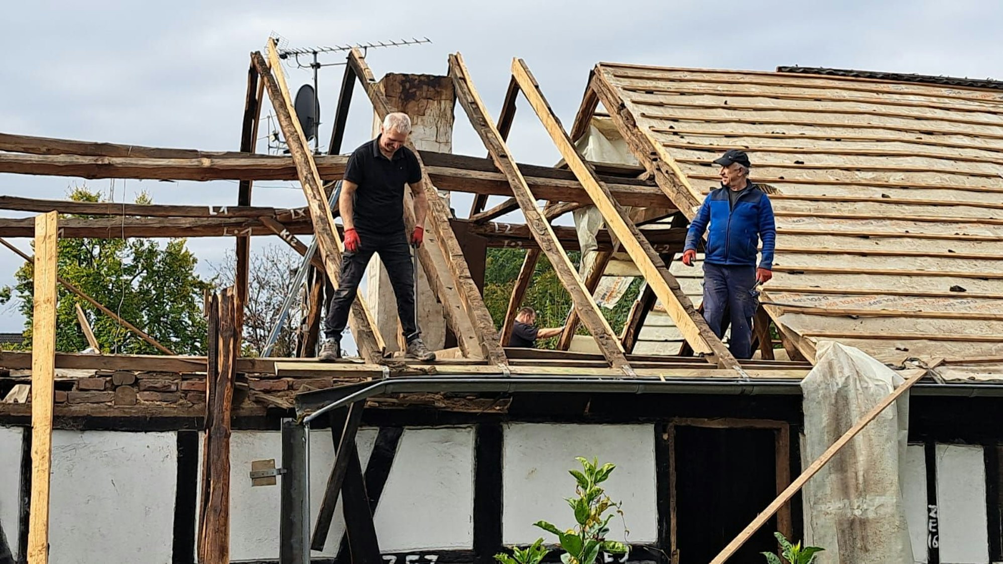 Ein Dachstuhl wird von zwei Männern abgebaut.