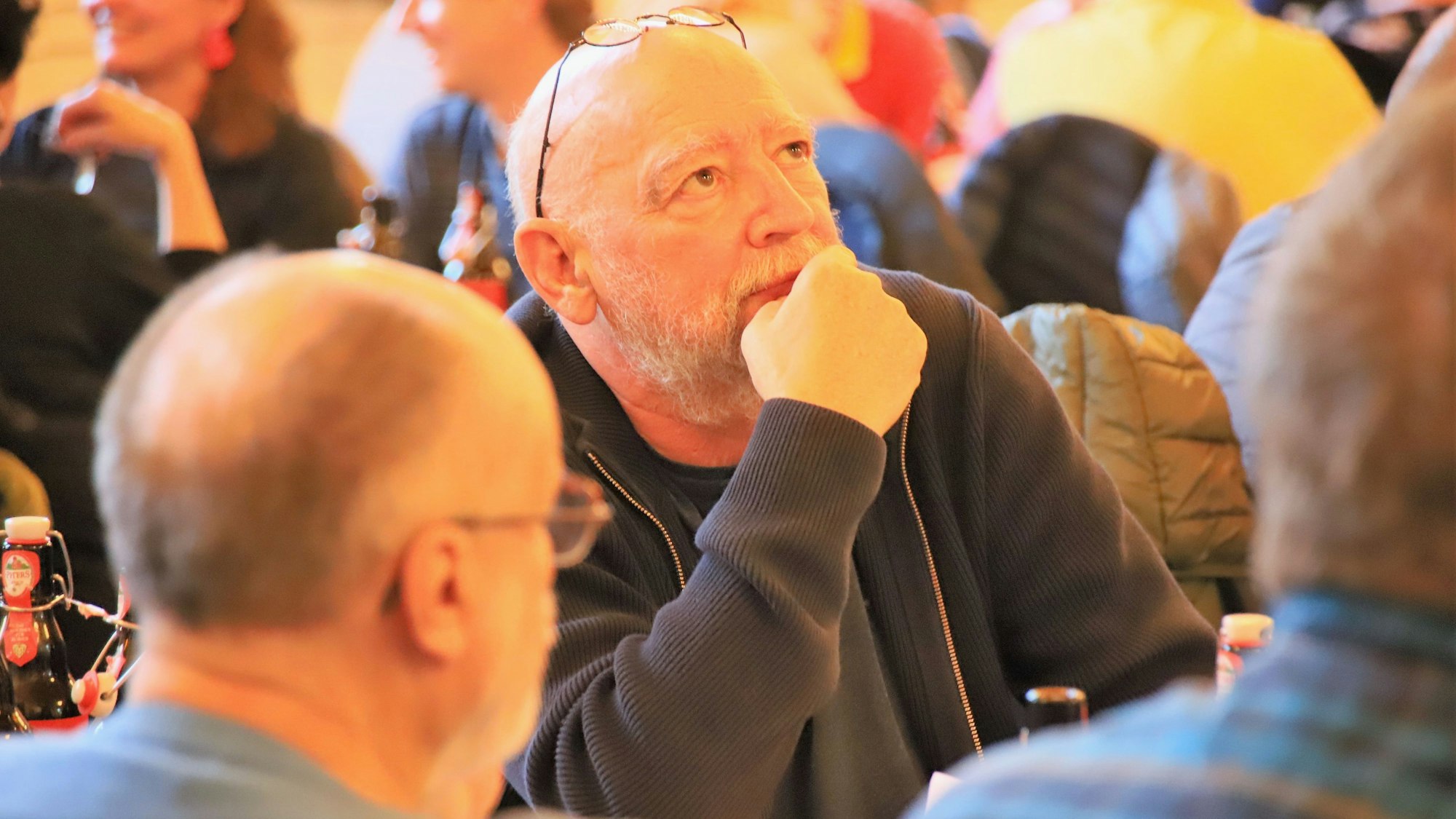Ein Mann mit Brille an einem Tisch; er schaut nach oben, die Brille hat er auf den Kopf geschoben.