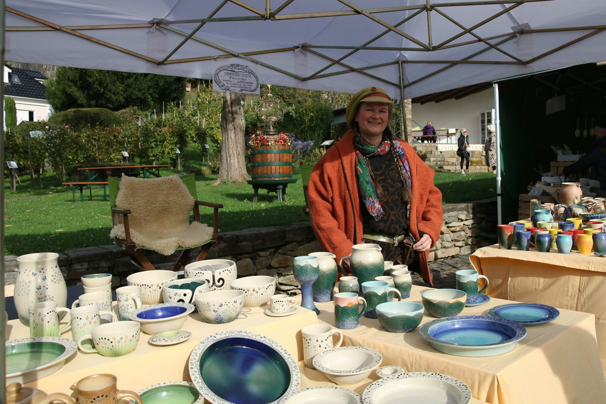Eine Frau in roter Jacke mit einem Stand mit Töpferwaren.