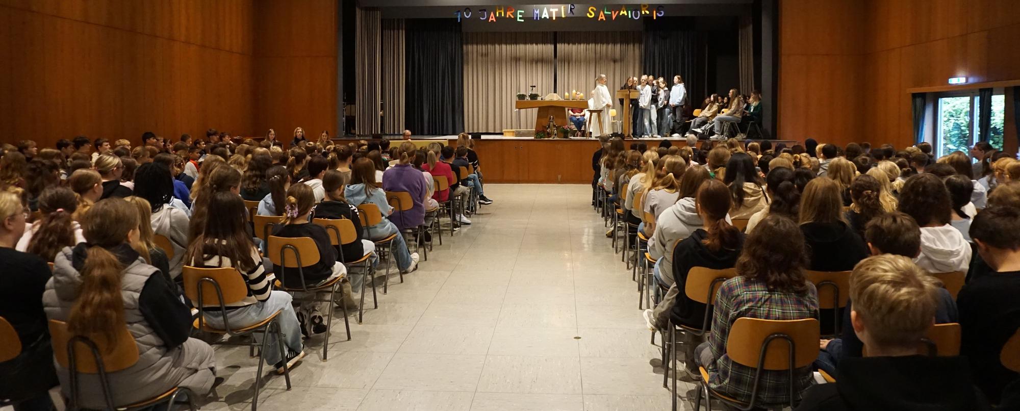 Das Bild zeigt einen Saal voller Schülerinnen und Schüler vor einer Bühne.