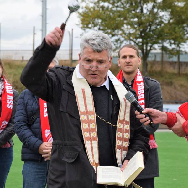 Ein Pfarrer segnet einen Fußballplatz.