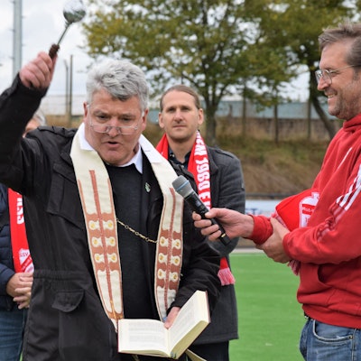 Ein Pfarrer segnet einen Fußballplatz.
