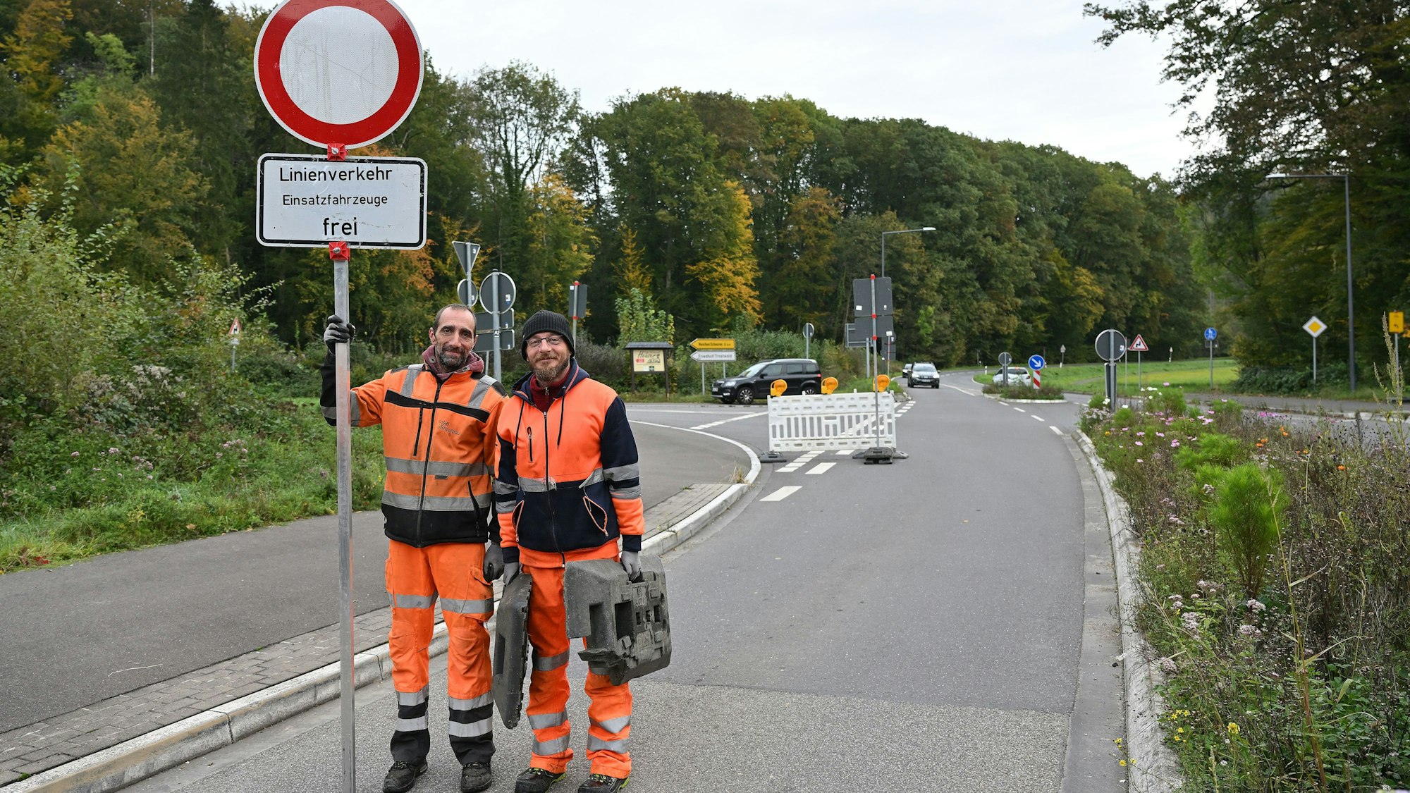 Zwei Mitarbeiter einer Baufirma halten ein Schild "Durchfahrt verboten" hoch. Darunter steht "Linienverkehr und Einsatzfahrzeuge frei".
