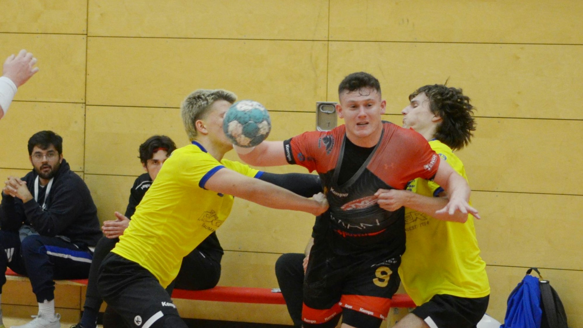 Schmitz, mit dem Ball in der rechten Hand, wird von zwei Abwehrspielern hart bedrängt.