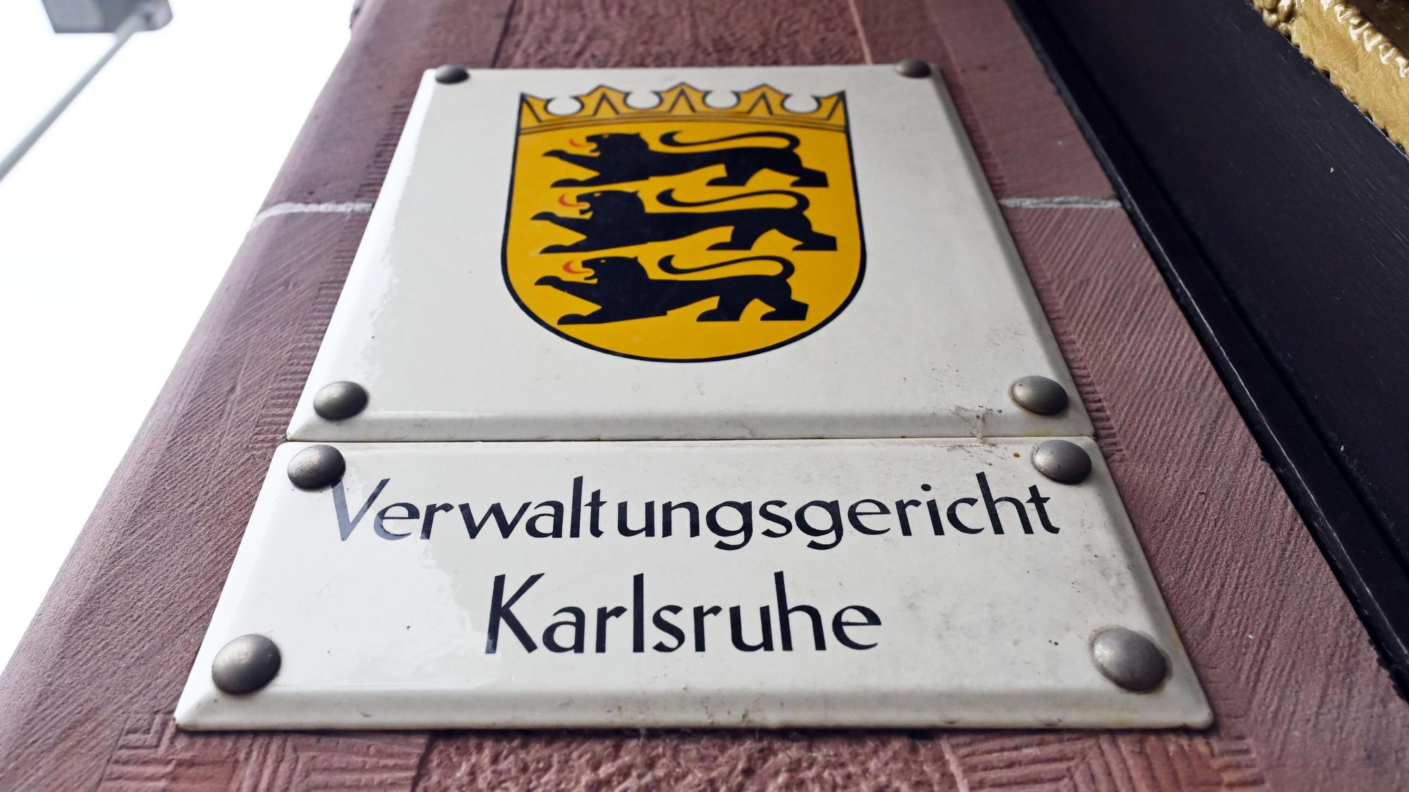 Ein Hinweisschild mit dem Landeswappen von Baden-Württemberg und dem Schriftzug ·Verwaltungsgericht Karlsruhe·, aufgenommen vor dem Gericht.