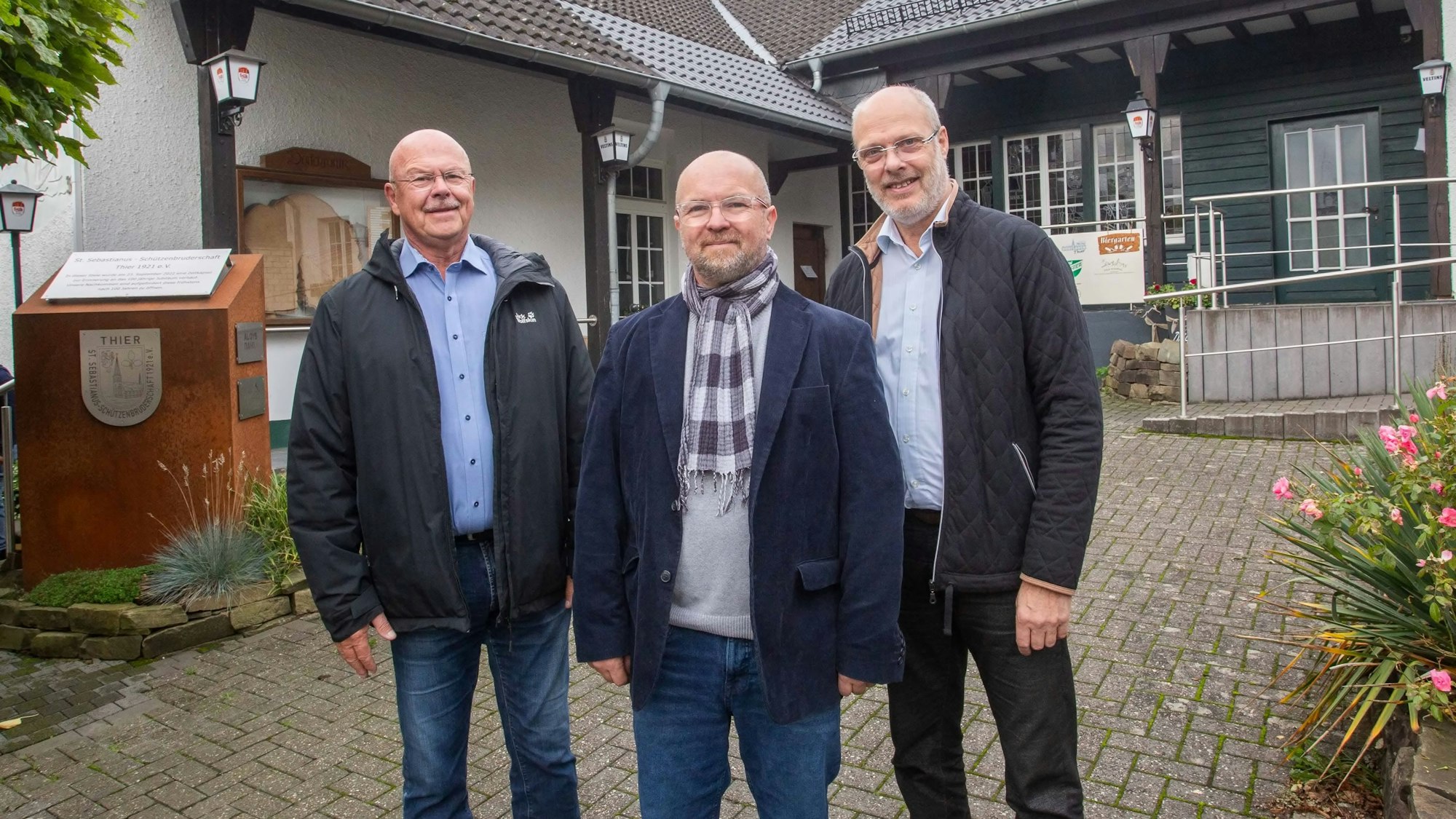 Vor dem Dorfgemeinschaftshaus in Thier stehen drei Männer und schauen in die Kamera.