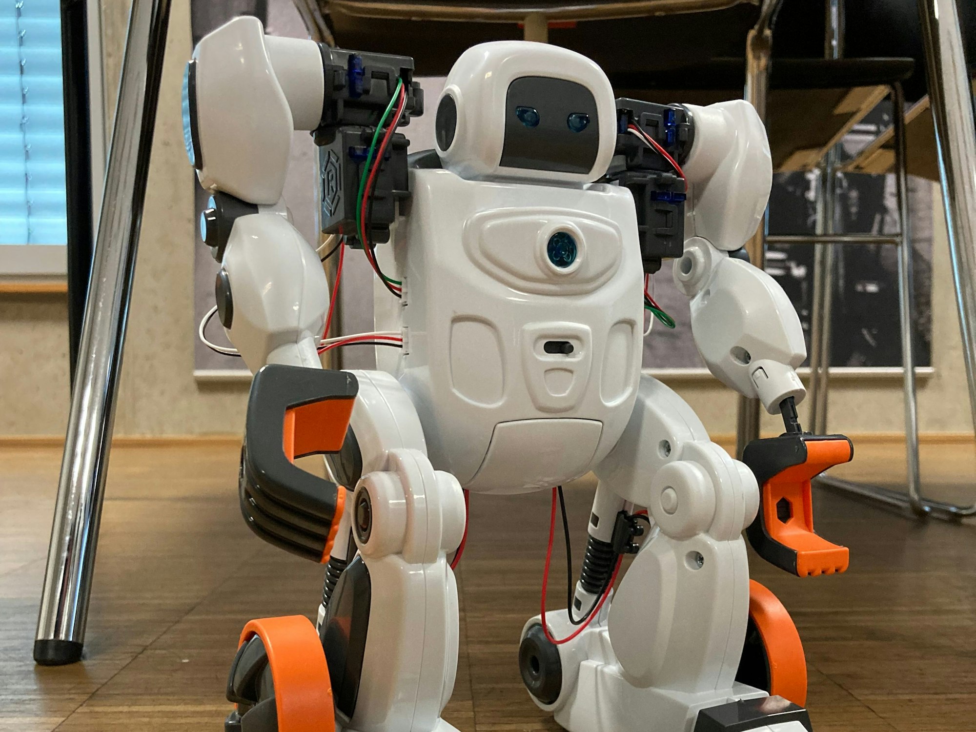 Ein Roboter steht vor einem Stuhl auf dem Boden.
