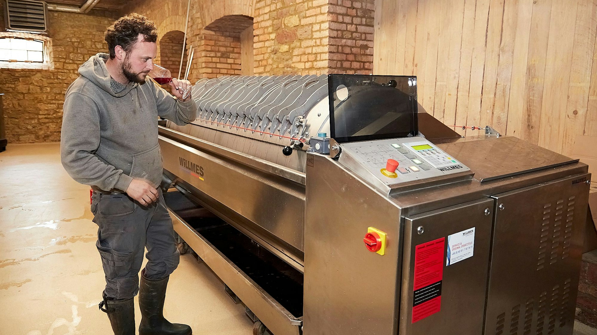 Markus Schäfer steht in einem Raum in einem alten Gebäude. Er reicht an einer roten Flüssigkeit in einem Weinglas.