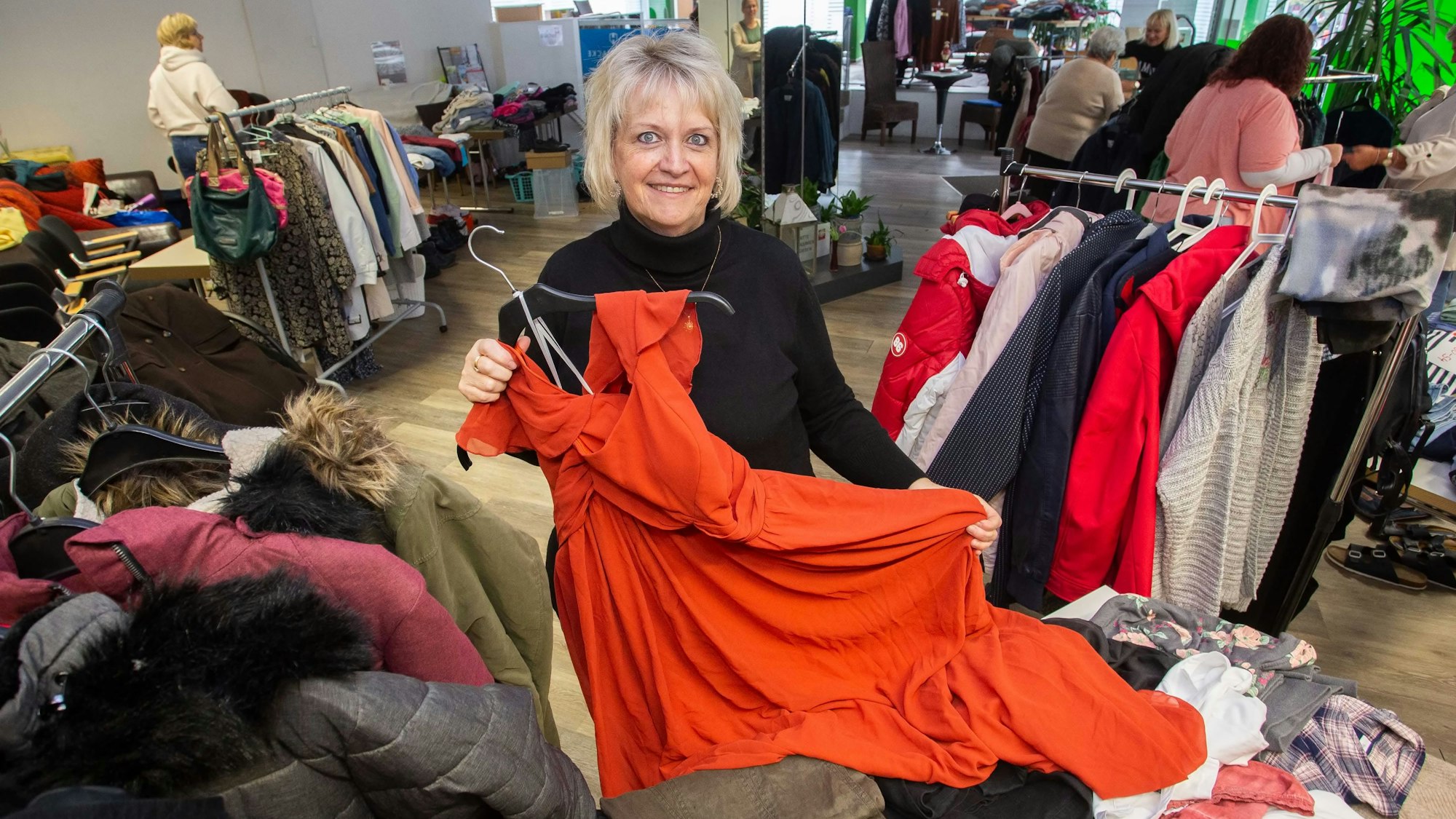 Eine Frau hält auf einem Secondhandmarkt ein rotes Kleid in einer großen Größe in den Händen.