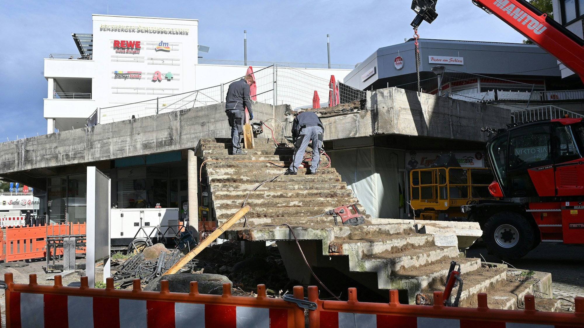 Man sieht die abgetrennte Betontreppe. Zwei Bauarbeiter stehen auf den oberen Stufen.