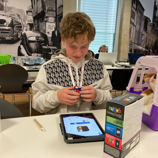 Ein Junge dreht einen Zauberwürfel und schaut dabei auf ein Tablet.