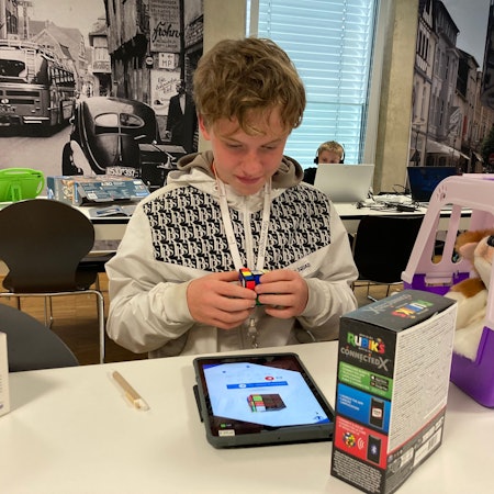 Ein Junge dreht einen Zauberwürfel und schaut dabei auf ein Tablet.