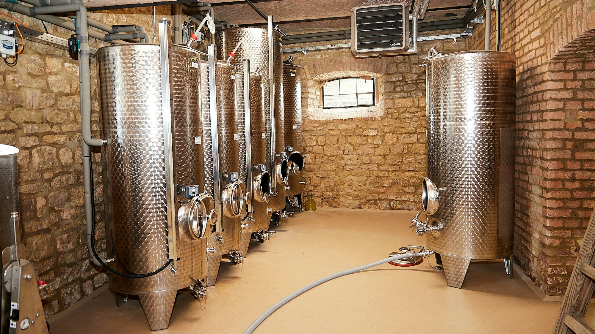 Mehrere hohe Edelstahlfässer stehen in einem mit Bruchsteinen gemauerten Raum.