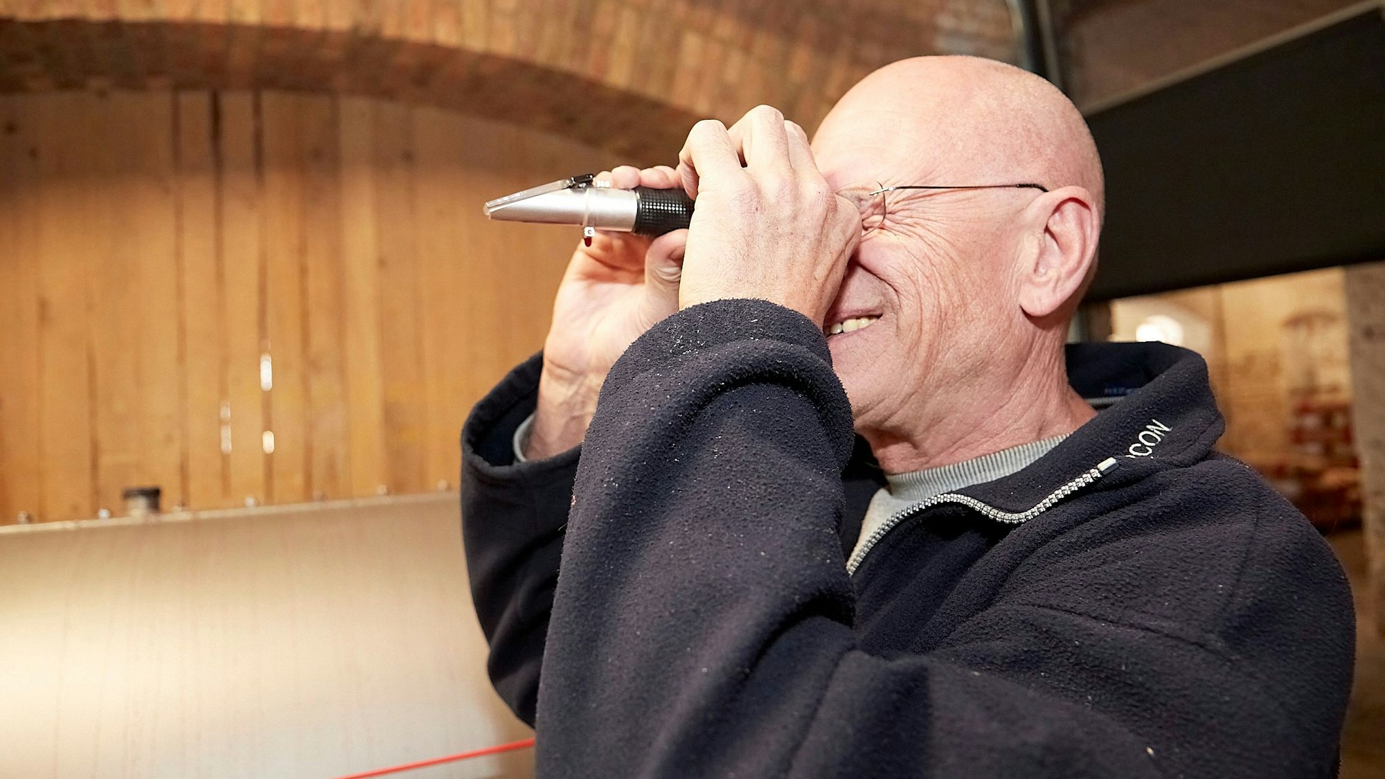 Heinz Bechtold hält sich ein silber-schwarzes Gerät vor das rechte Auge. Er schaut durch das Refraktometer, um den Zuckergehalt zu messen.