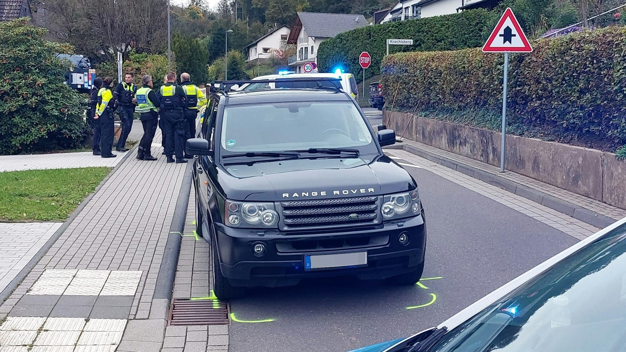 Ein Range Rover steht in Hennef auf einer Straße, die Fahrbahn ist markiert, Polizisten stehen im Hintergrund.