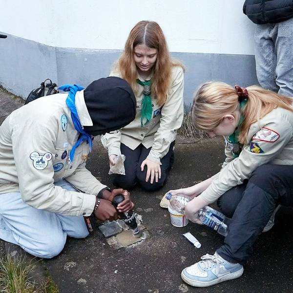Drei Jugendliche in Pfadfinderhemden hocken auf dem Boden. Sie reinigen mehrere Stolpersteine, mit denen an von den Nationalsozialisten ermordete Mitbürger erinnert wird.