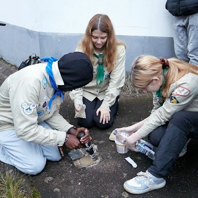 Drei Jugendliche in Pfadfinderhemden hocken auf dem Boden. Sie reinigen mehrere Stolpersteine, mit denen an von den Nationalsozialisten ermordete Mitbürger erinnert wird.