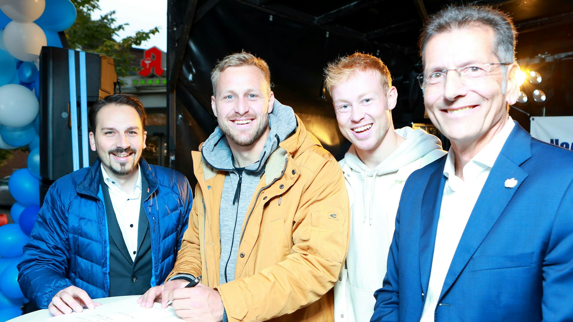 Vier Männer lachen in die Kamera, einer hält einen Stift in der Hand.