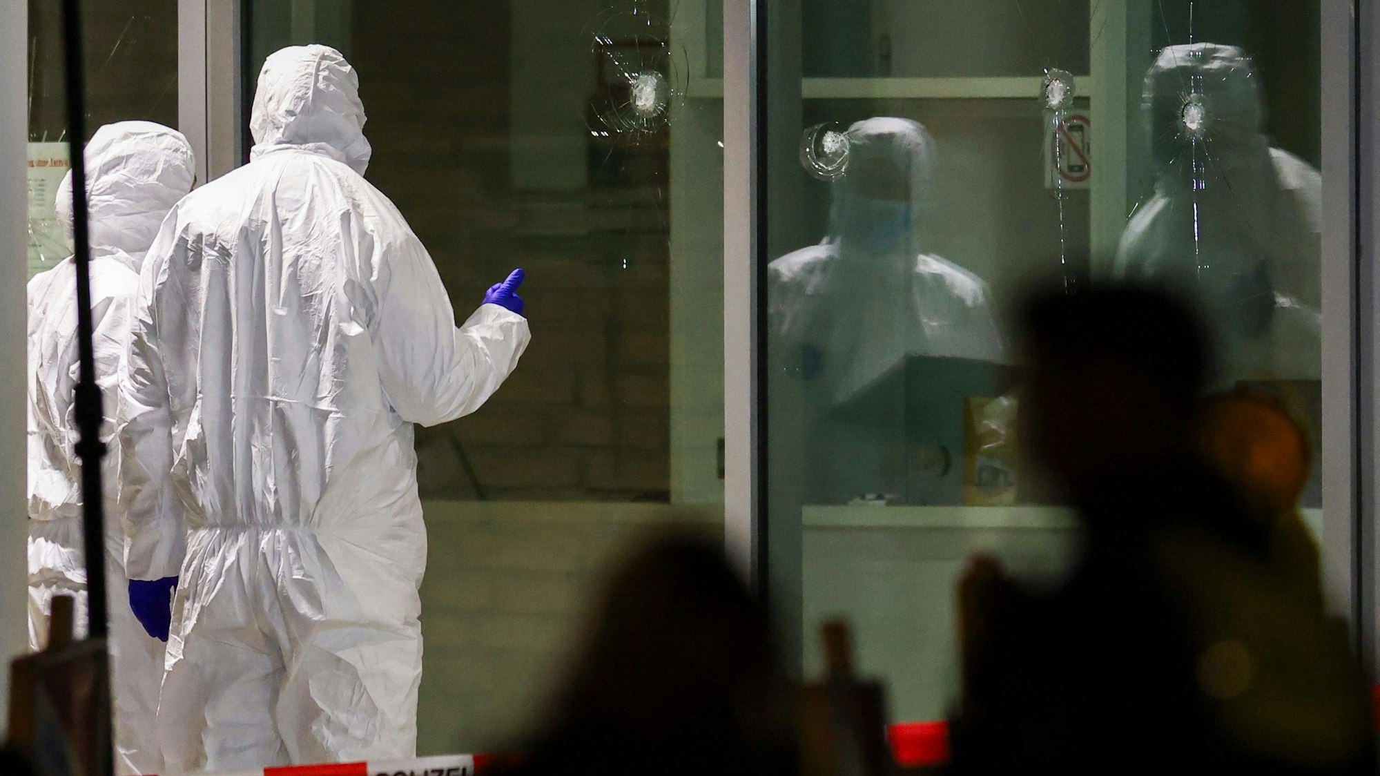 Krefeld: Polizeibeamte der Spurensicherung in weißen Schutzanzügen untersuchen Löcher in Glasscheiben des Kinos. Im Foyer eines großen Kinos am Hauptbahnhof in Krefeld hat die Polizei einen Verdächtigen niedergeschossen.