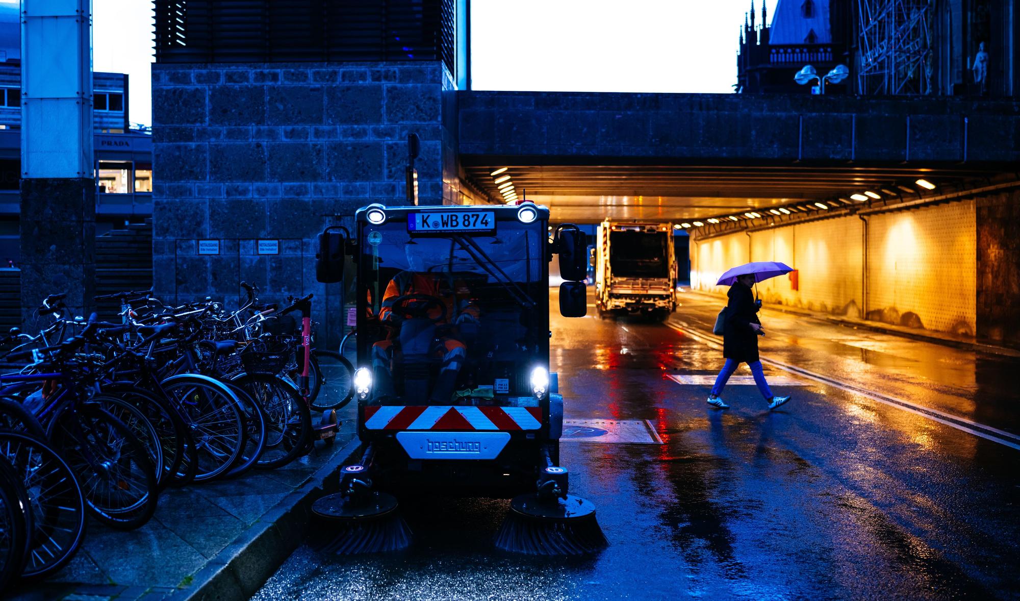 Eine Kehrmaschine fährt in der Dämmerung über eine Straße.