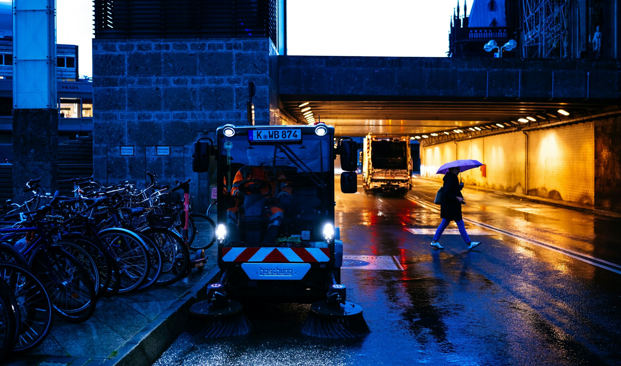 Eine Kehrmaschine fährt in der Dämmerung über eine Straße.