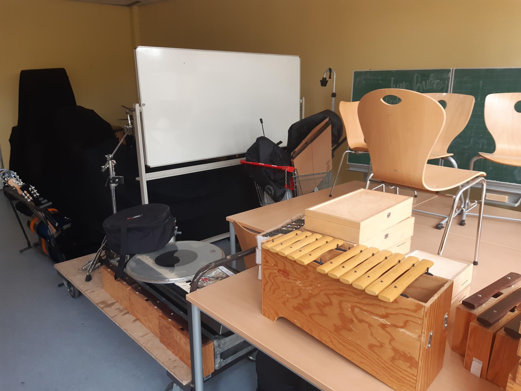 Das Bild zeigt einen Klassenraum, der mit Musikinstrumenten vollgestellt ist.