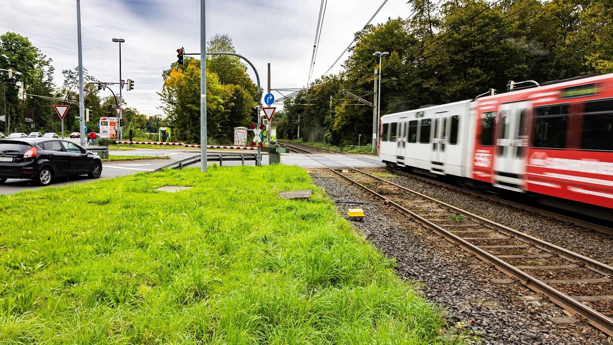 Autos stehen an einer Schranke und eine Straßenbahn fährt an ihnen vorbei.