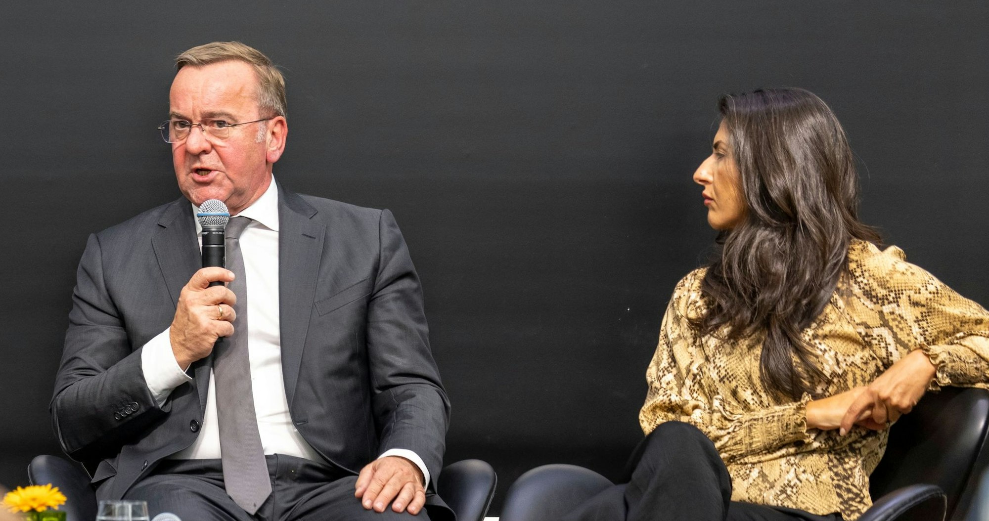 Boris Pistorius spricht in ein Mikrofon, neben ihm sitzt Serap Güler.